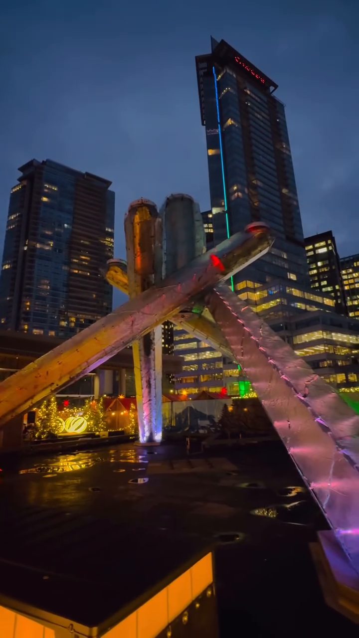 Vancouver towers at dusk with the colorful Olympic Cauldron in front